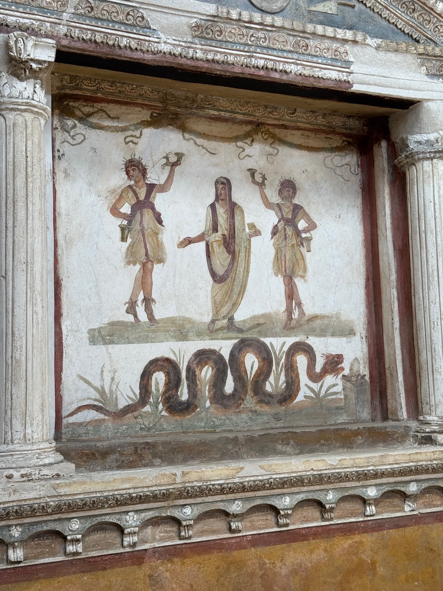 Two dancing lares, or household gods with a genius, another type of god in the middle, representing the head of the household. The serpent at the bottom, which symbolized prosperity.