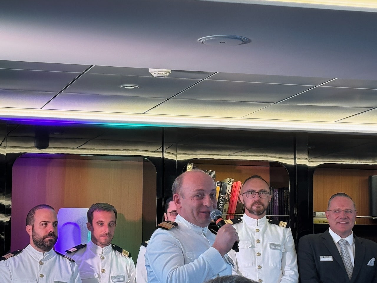 Captain Yevgeniy Lebedenko World Traveller, Atlas Ocean Voyages holding a microphone with crew members behind him.